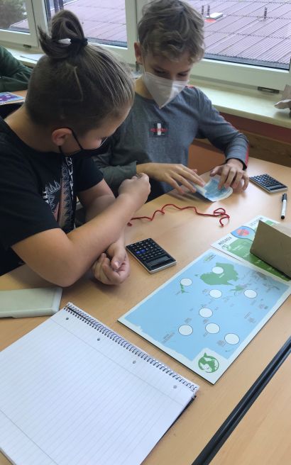 Zwei Schüler beugen sich über eine Aufgabe mit Taschenrechner und Landkarte.
