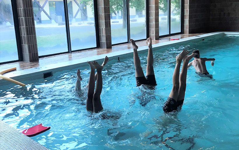 Fünf Kinder machen in einem Schwimmbad einen Handstand unter Wasser. Es schauen nur die Beine heraus.