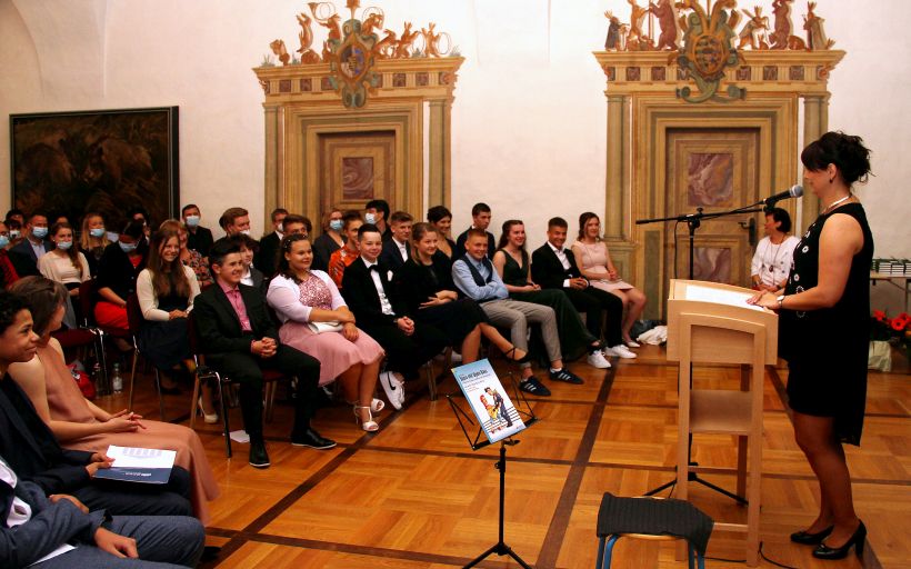 Schüler:innen sitzen in einem festlichen Saal des Schlosses Augustusburg und lauschen der Rede der Schulleiterin.